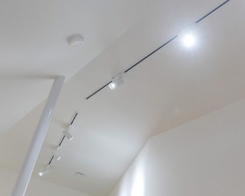 Katto, jossa on valkoinen, minimalistinen muotoilu ja useita LED-kiskovalaisimia, tulee yksi loistaa kirkkaasti. Kattoon on kiinnitetty myös pieni, pyöreä palovaroitin. Huone vaikuttaa moderniilta ja siistiltä. Tämä sopii hyvästi. LedStorefi:n laaduseen led-valaistusvalikoimaan.