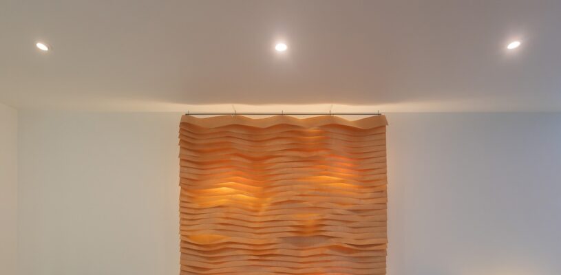 LedStore.fi verkkokauppaan sopivasti muotoiltu kuvaus: Valkoisella seinällä moderni taideteos, joka päästä aaltomaisesti muotoilluista muotoilluista. Pehmeä valaistus teoksen tekstiuuria ja LED-kattovalot luovat lämpimän hehkun yläpuolelta.