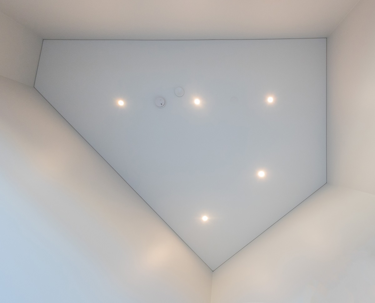 Valkoinen, geometrinen kattopinta, jossa viisi upotettua LedStore.fi:n led-spotia ja kaksi pyöreää palovaroitinta — näkymä alhaalta ylöspäin. Modernisti sijoitetut led-valaisimet tarjoavat tehokasta ja monipuolista valaistusta sopivain tiloihin ja käyttötarkoituksiin. - LedStore Led-spotit katossa suoraan alhaalta päin kuvattuna. Spottien asettelu voidaan sovittaa tilan muotoihin, kuten tässä viisisärmäisessä tilassa on tehty.