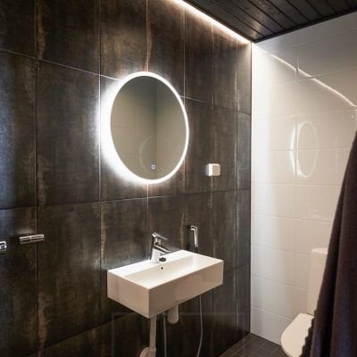 Tumma kylpyhuone valaistu tunnelmallisesti spottivalaistuksella ja epäsuoralla valolla. Valopeilissä on huurunpoistotoiminto joka pitää peilin kirkkaana saunasta tai suihkusta tullessa. Ledstore.fi