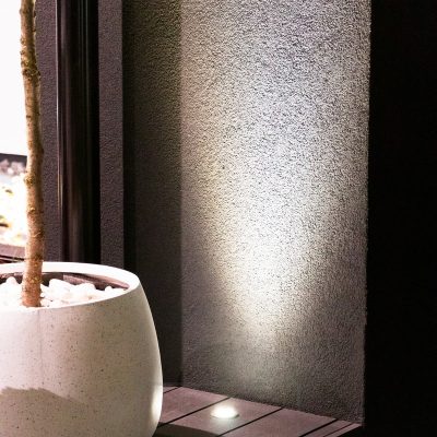 Ylöspäin valaiseva terassiin upotettu spotti valaisemassa seinän kautta. Valo myös korostaa kauniisti edessä olevaa kasvia. Ledstore.fi
