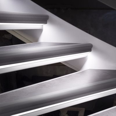 Yksityiskohtainen näkymä kelluvasta portaikosta, jossa on tyylikäs LED-valolista, korostusvalaistus ja valkoinen seinä.