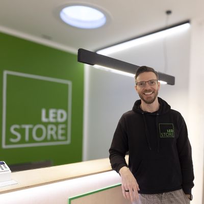 A man i LED STORE-huvtröja vid belysningsdisk, grön LED-skylt, moderni butiksmiljö