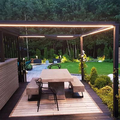 Moderni patio, jossa on betonipöytä, penkit ja LED-valaistus puisella terassilla, jota ympäröi vehreä puutarhatunnelma.