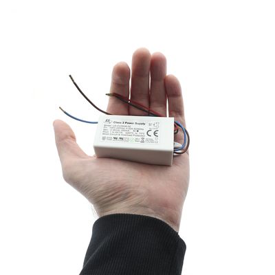Käsi pieni suorakaiteen muotoinen LED-virtalähde, jossa johdot näkyvät, valkoinen tausta. Energiatehokas valaistusratkaisukomponentti.