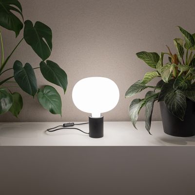 Moderni LED-pöytävalaisin, jossa valkoinen pyöreä varjostin hyllyllä, vihreiden ruukkukasvien ympäröimänä tyylikkääseen kodin valaistukseen.