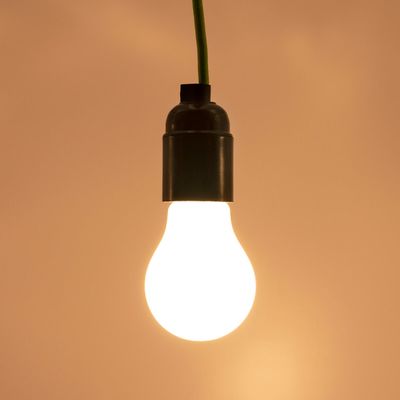 LED-lamppu vihreällä johdolla, hehkuu lämpimästi ruskeaa taustaa vasten. Ihanteellinen energiatehokkaisiin valaistusratkaisuihin ja tunnelman parantamiseen.
