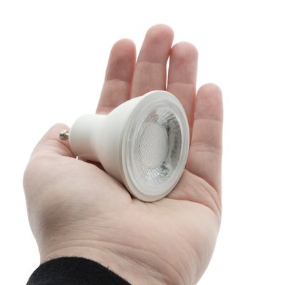 Kädessä pieni pyöreä LED-lamppu valkoisella pohjalla korostaen energiatehokkaita valaistusratkaisuja LED-myymälästämme.