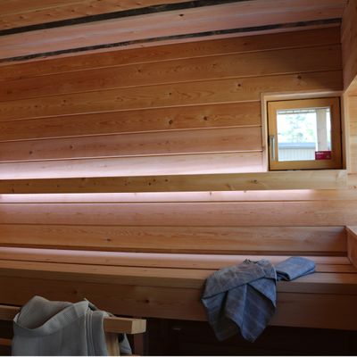LED-valaistu puinen saunasisustus lauteilla, pieni ikkuna ja pyyhkeet; täydellinen valaistus rentouttavaan kylpyläkokemukseen.