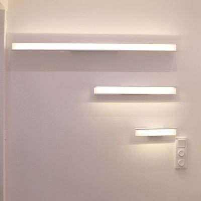 Kolme kasvavaa kokoista vaakasuoraa suorakaiteen muotoista seinävalaisinta valkoisella seinällä, valokytkin pienimmän alla. Moderni LED-valaistussuunnittelu.