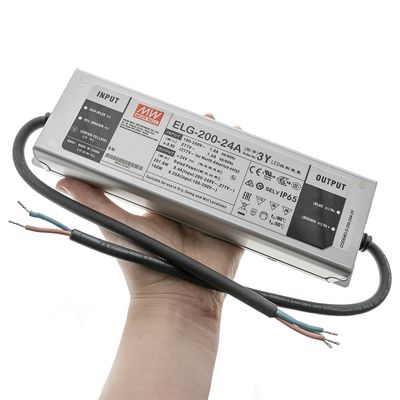 Lähikuva kädessä pitävästä Mean Well ELG-200-24A LED-ohjaimesta näkyvillä tulo- ja lähtöjohdoilla, ihanteellinen energiatehokkaisiin LED-valaistusratkaisuihin.