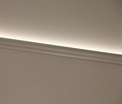 Moderni valkoinen jalkalista, jonka yläpuolella on hienovarainen LED-valotehoste, joka valaisee seinää, mikä korostaa puhdasta ja nykyaikaista muotoilua.