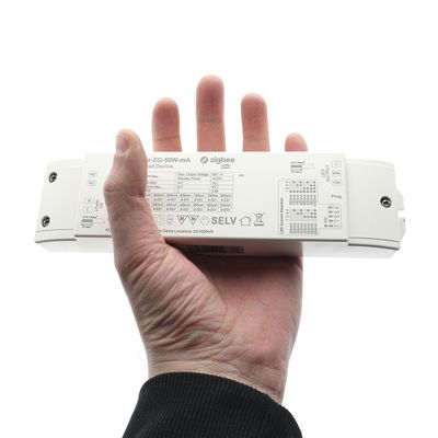 Kädessä valkoinen suorakaiteen muotoinen laite, joka näyttää tekniset tiedot ja symbolit sekä sana "Zigbee", joka liittyy LED-valaistustekniikkaan.