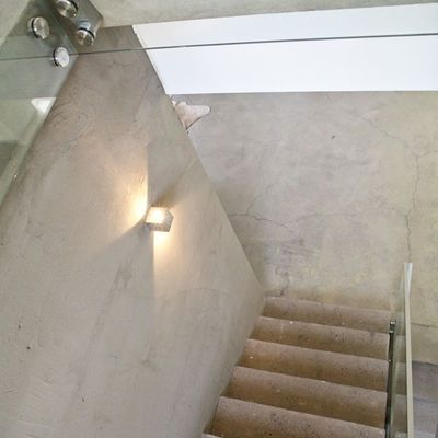 Moderni portaikko, jossa on betoniportaat, lasikaide ja seinään asennettava LED-valo, joka loistaa lämpimästi; minimalistinen muotoilu lisää tunnelmaa.