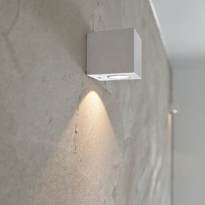 Minimalistinen seinään kiinnitettävä neliönmuotoinen LED-valaisin, joka luo lämpimän hehkun teksturoituun harmaaseen seinään moderniin sisävalaistukseen.