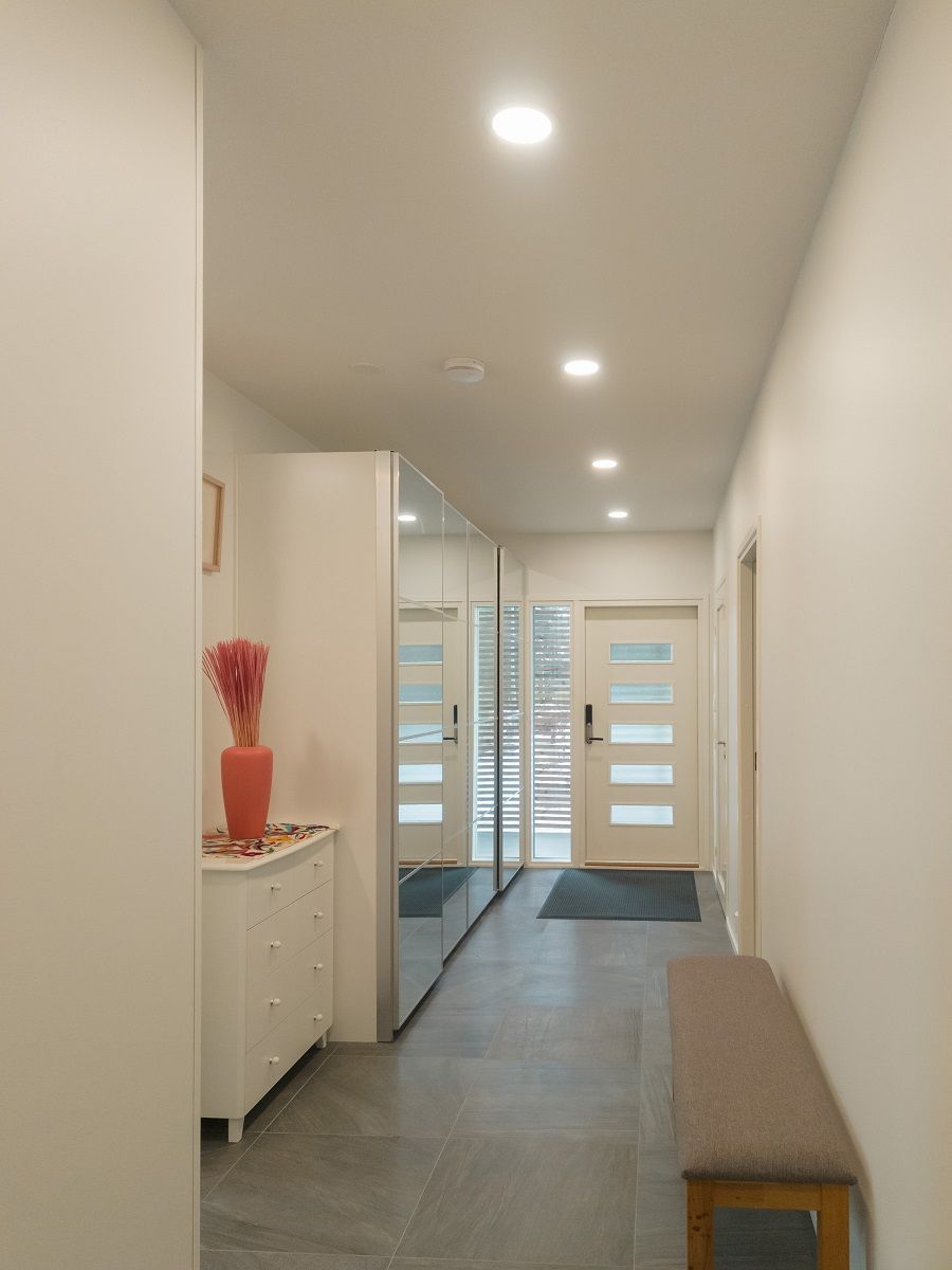 Vaalea eteiskäytävä on valaistu pienillä pyöreillä paneelivalaisimilla.