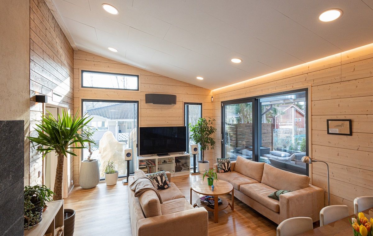 Olohuone, jossa vaaleat puupinnat ja vaalea katto. Katossa uppoasennettuna pyöreitä paneelivalaisimia ja led nauha seinän ja katon rajassa.