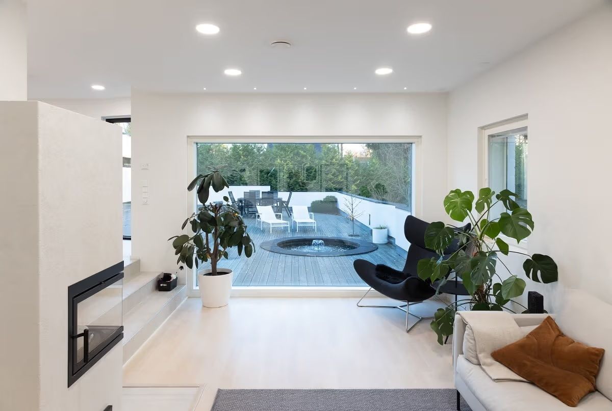 Vaaleapintainen olohuone, jossa suuresta ikkunasta näkyy ulos. Katossa näkyy pyöreitä led paneeleita ja pieniä spottivaloja ikkunan edustalla.