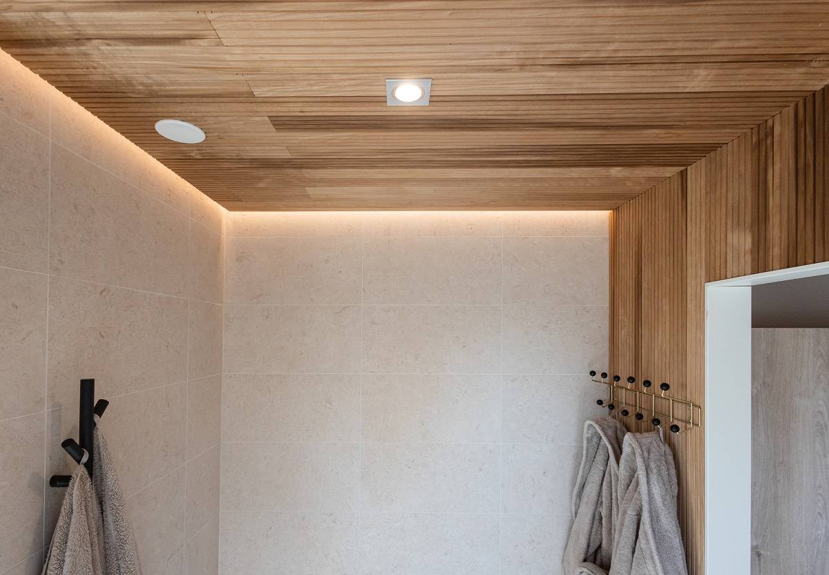 LedStore.fi tarjoaa moderniin kylpyhuoneeseen ratkaisun nykyaikaisella led-valaistuksella. Beigeillä laatoilla koristellut seinät, puinen säkatto ja upotettu LED-valaistus luovat näin ja raikkaan ilmeen. Mustille ripustetut koukuille pehmeät harmaat pyyhkeet hienot minimalistisen sisustuksen harmonisesti.