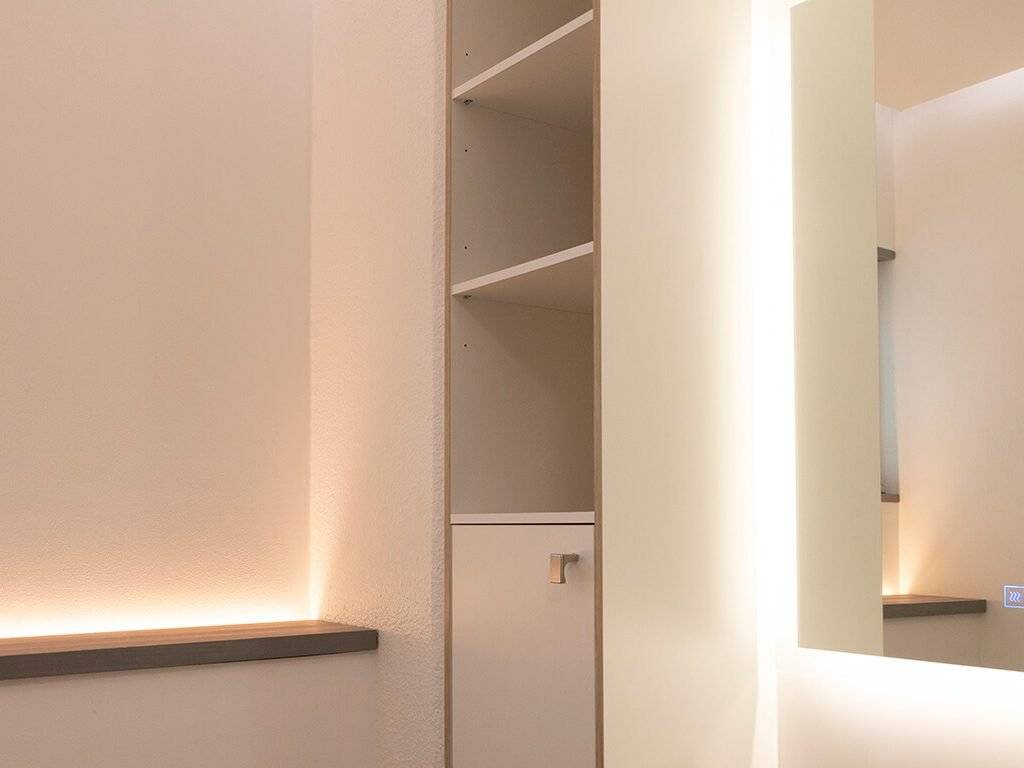 Minimalistinen sisustus, modernit LED-valaistut hyllyt, peilattu seinä, pehmeä valaistus. Neutraalit värit ja selkeät linjat luovat tyylikkään ja tyylikkään tilan.