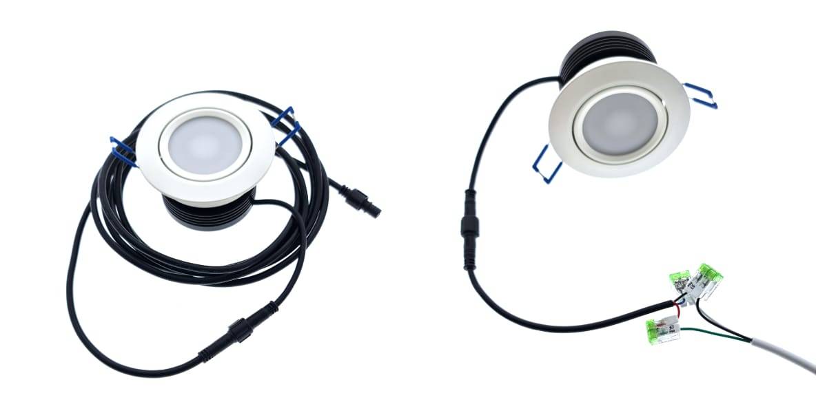 Kaksi pyöreää LED-alasvaloa, joissa on valkoiset kehykset, on kiinnitetty pitkiin mustiin johtoihin. Valoissa on liittimet johtojen päissä. Toinen johto on kierretty, kun taas toinen ulottuu ja yhdistyy vihreisiin riviliittimiin korostaen oman tyylikkään LED-integraatiota.