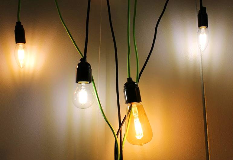 Neljän tyylikkään LED-lampun mustat ja vihreät johdot roikkuvat vaaleaa seinää vasten, moderniin sisustukseen.