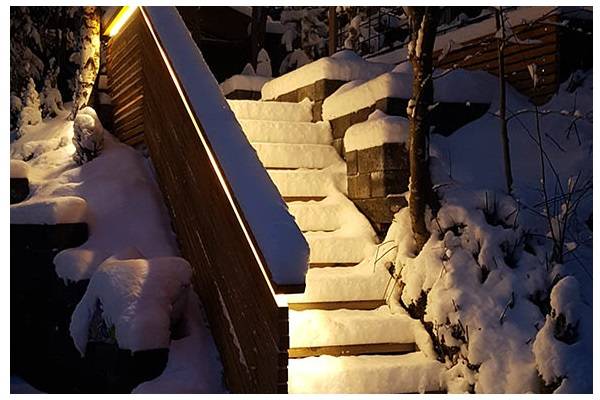 Lumiset portaat iltahämärässä, kaiteesta kajastaa lämpimän sävyistä valoa portaisiin. 